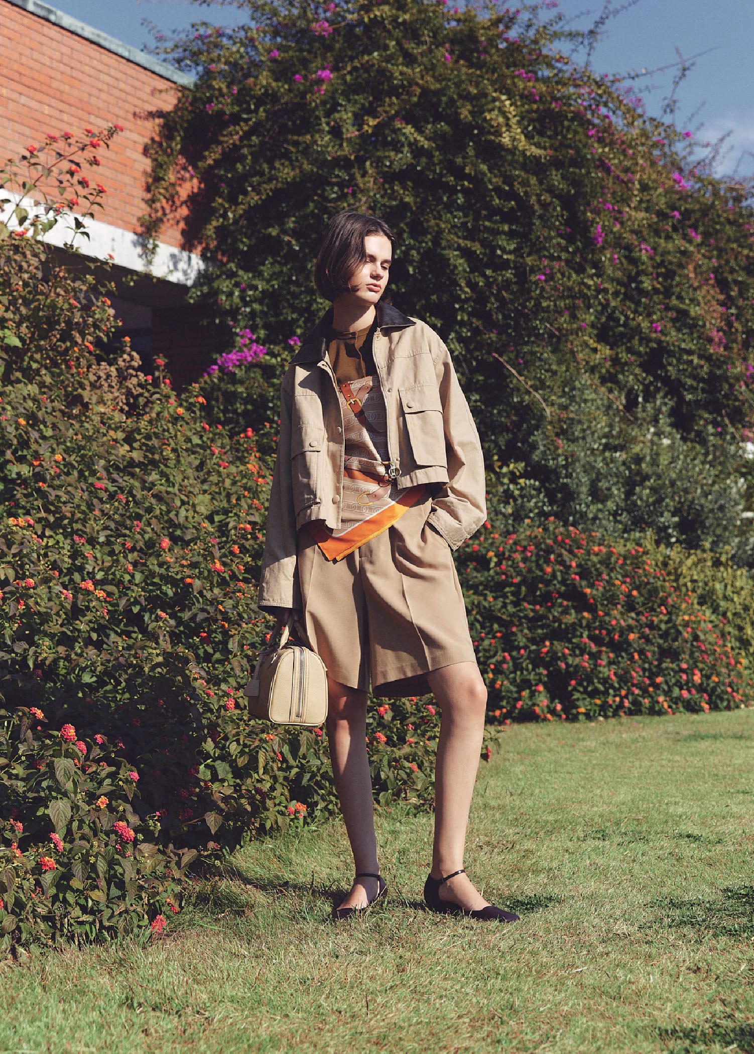 ショート丈テントシルエットハンティングJK&UVケアテレコボレロCD&トリミングハーフキュロットPT&ベルトモチーフ柄スカーフ&メタルドロップピアス&ショルダー付きボストンバッグ&アンクルストラップパンプスを着用した女性