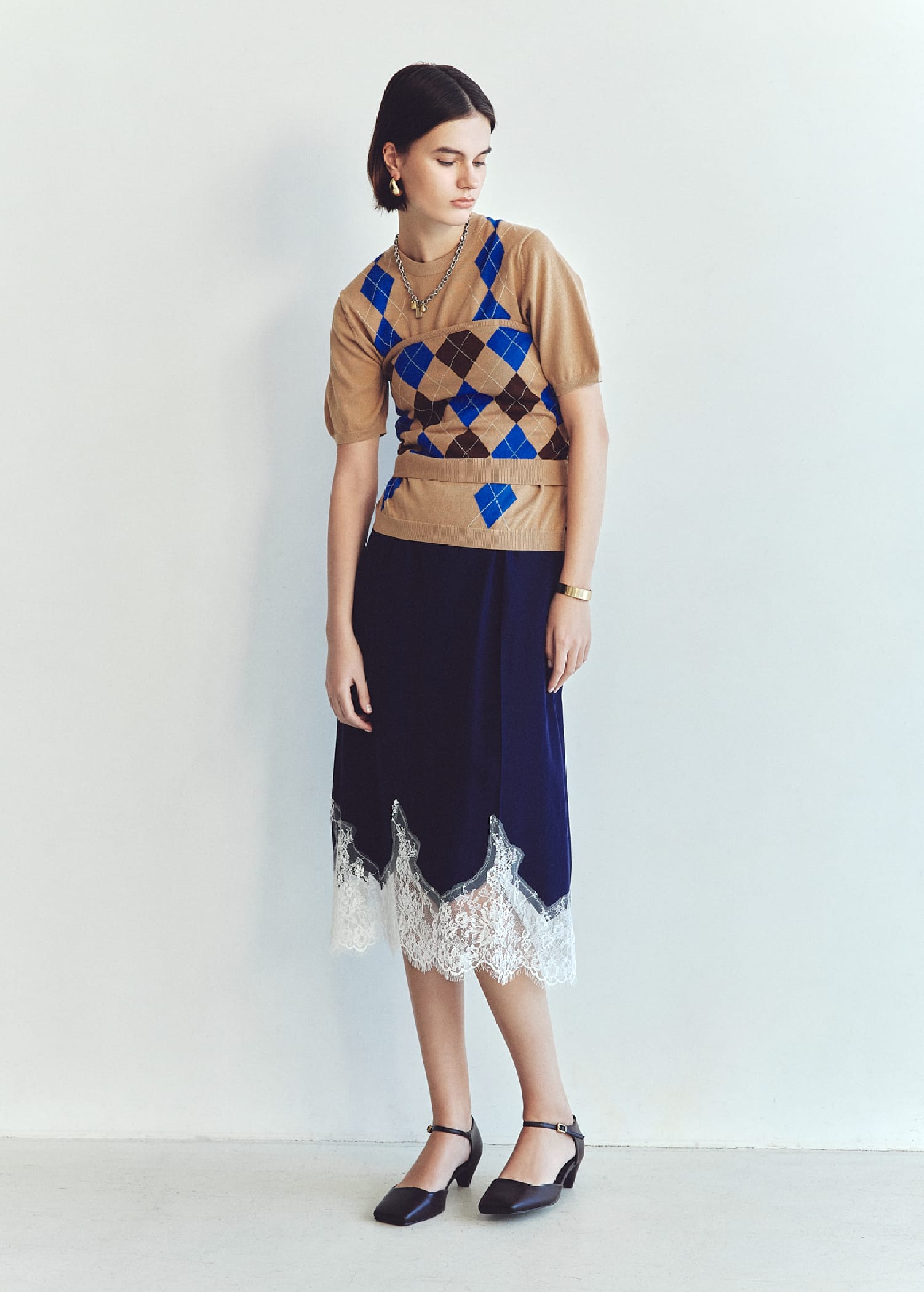 アーガイルニットトップス&アーガイルニットチューブトップ&レースヘムスカート&メタルドロップピアス&ランダムプレートチャームチェーンネックレス&カーブカラーバングル&アンクルストラップパンプスを着用した女性