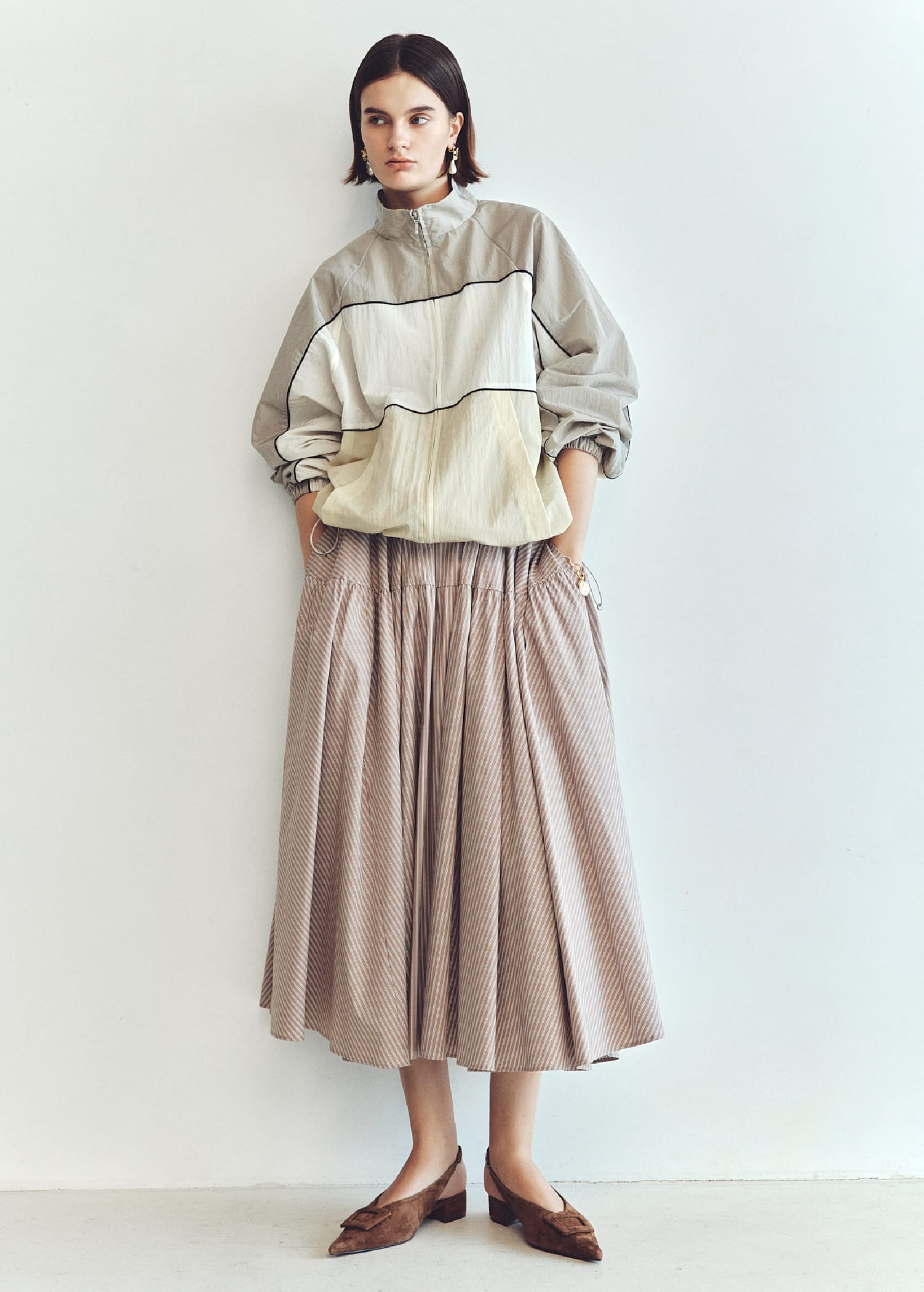 ナイロントラックジャケット&2サイズウエストボリュームフレアSK&メタルモチーフパールイヤリング&コインモチーフチェーンブレス&バックル付きラムレザースリングパンプスを着用した女性