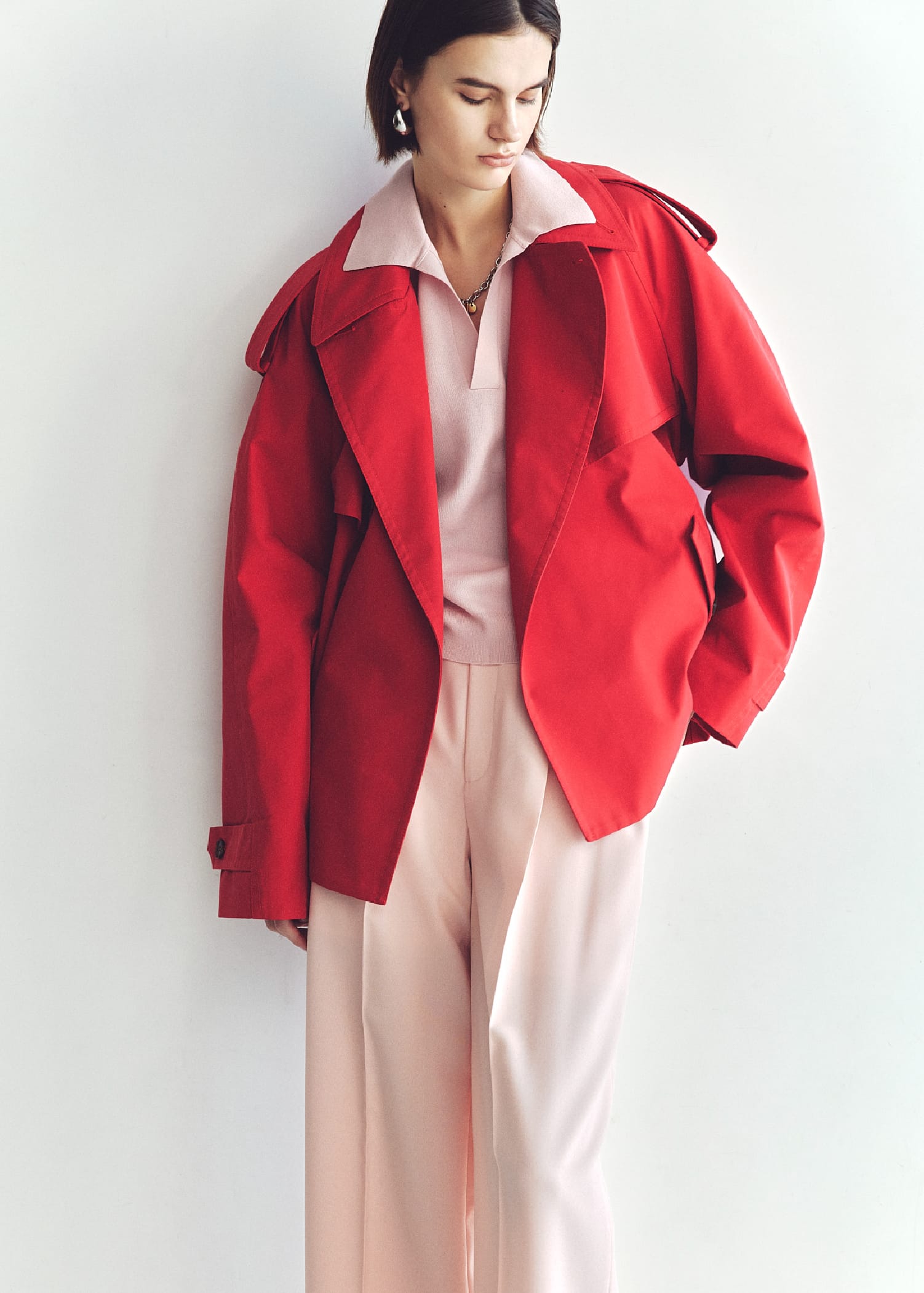 ショートトレンチコート&シアーポロニット&センタープレスイージーパンツ&メタルドロップピアス&モチーフチャームチェーンネックレス&トングサンダルを着用した女性