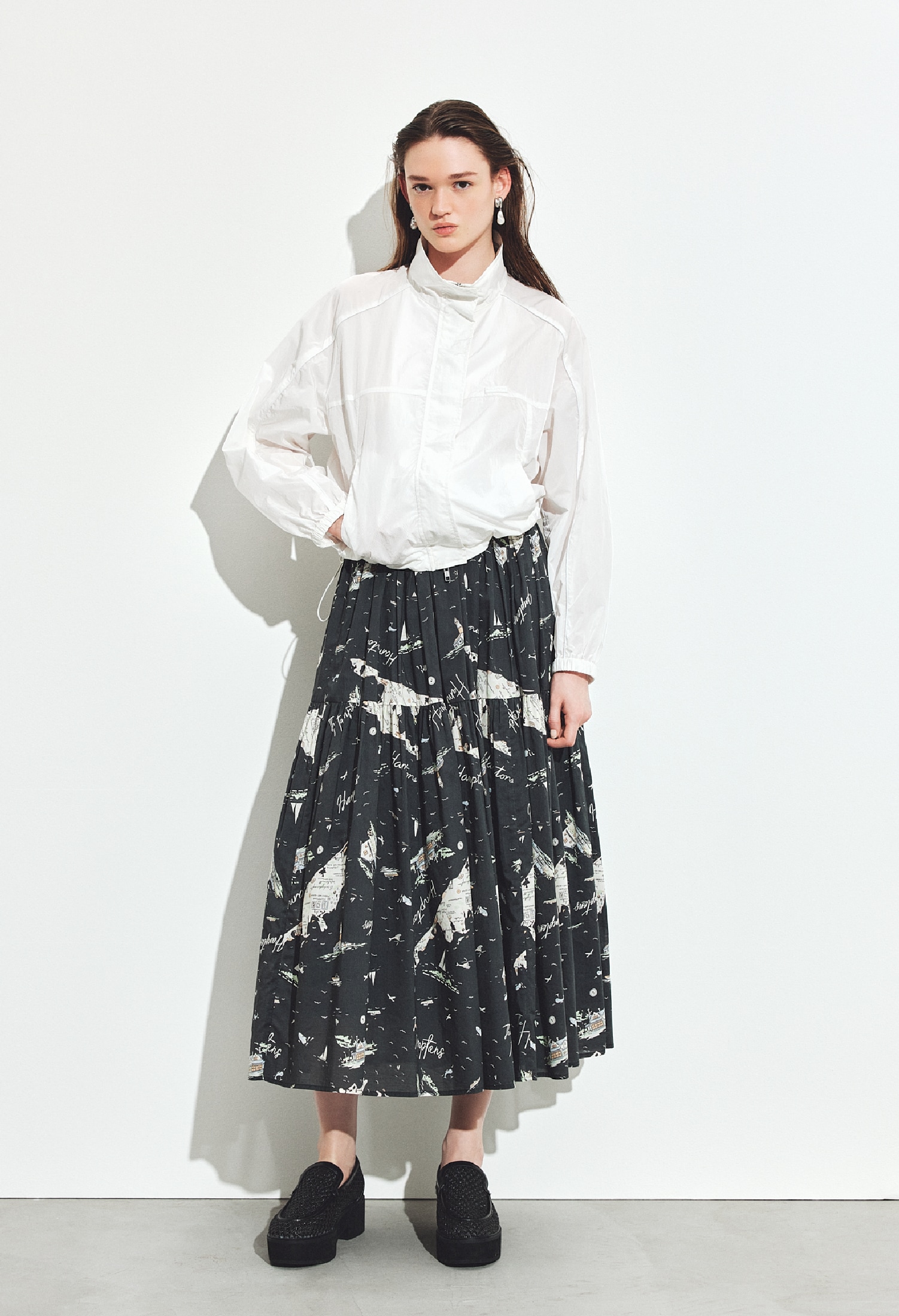 白のナイロントラックジャケット・チャコールグレーのティアードマキシスカート・シルバーのイヤリング・黒のメッシュローファーを合わせたコーディネート