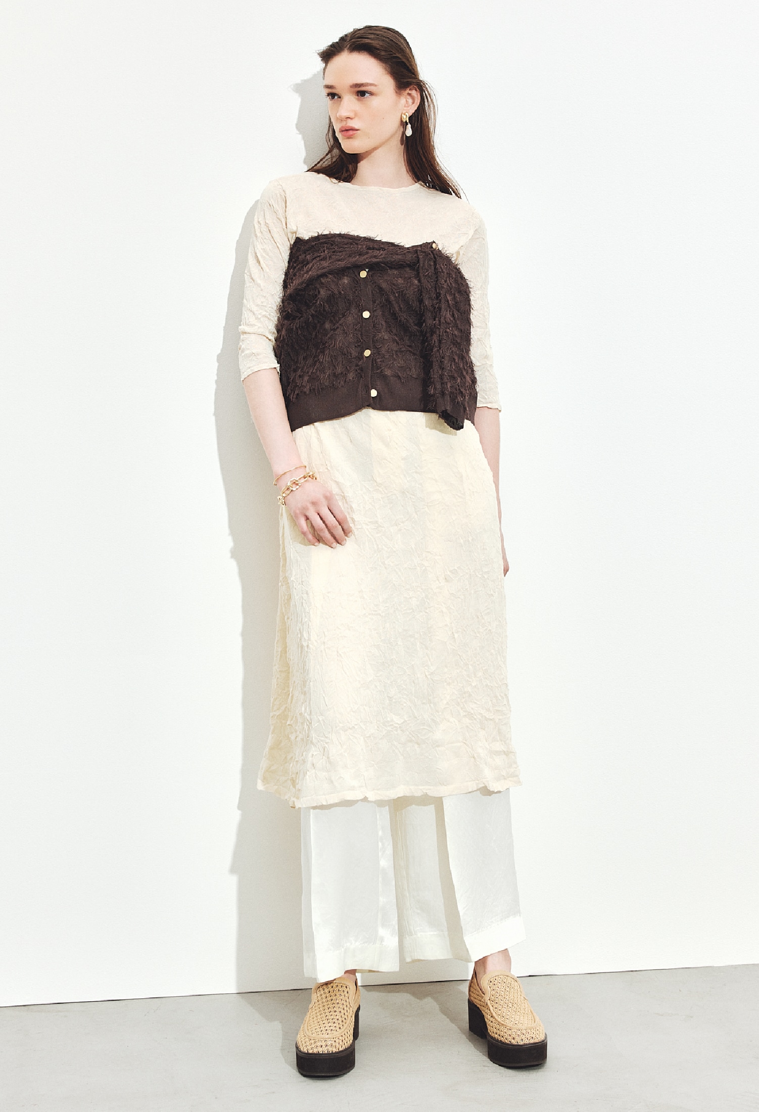 ライトベージュのバックオープンワッシャーニットワンピース・アイボリーのワイドスラックス・ダークブラウンのジャガードカーディガン・ゴールドのイヤリングとバングル・ベージュのメッシュローファーを合わせたコーディネート