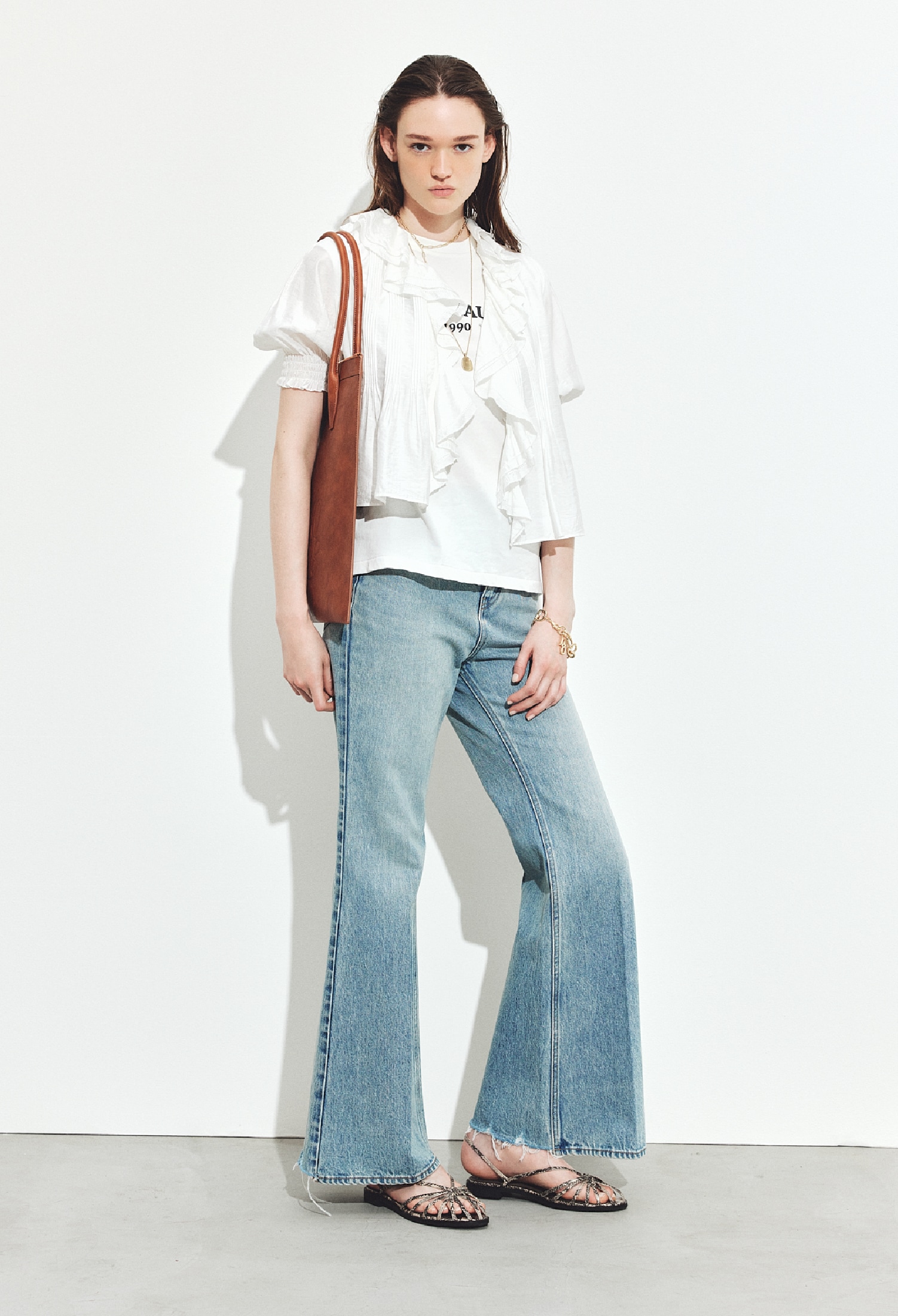 白のラッフルカラーブラウスとノースリーブTシャツ・ライトブルーのフレアデニム・ゴールドのネックレスとネックレスとブレスレット・キャメルのトートバッグ・ストラップサンダルを合わせたコーディネート