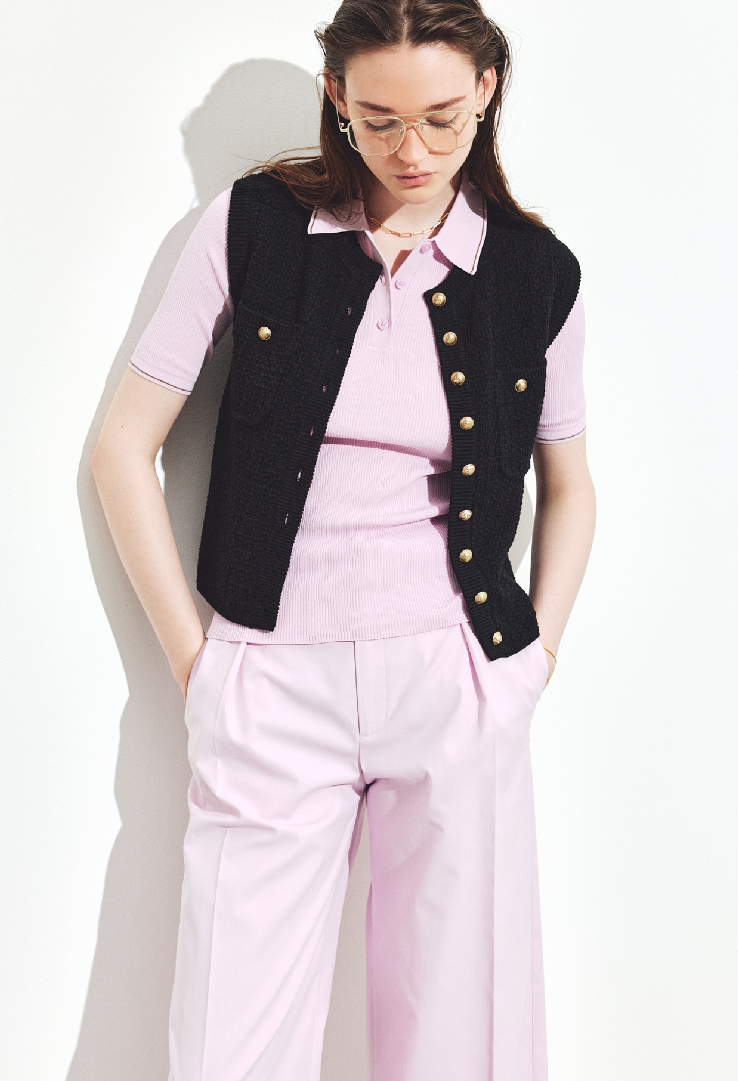 黒の金ボタンクロシェライクニットベスト・ピンクのシアーリブポロニット・ラベンダーのセミワイドタックパンツ・ゴールドのダテメガネとチョーカーとバングルを合わせたコーディネート