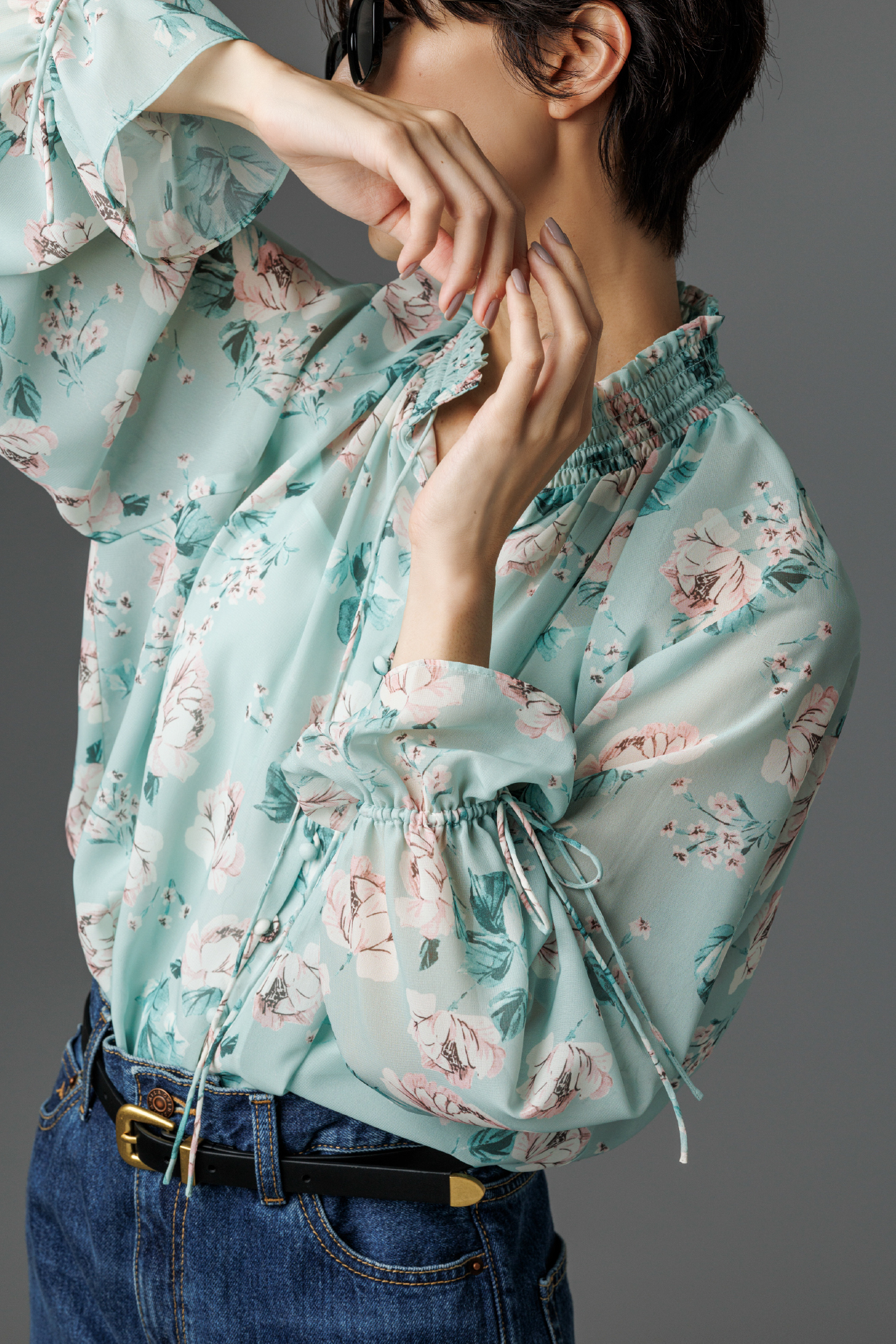 フラワープリントブラウス・ヘムデザインセミフレアデニムパンツ・メタルポイントセルフレームサングラス・ヴィンテージスリムベルトを着用した女性