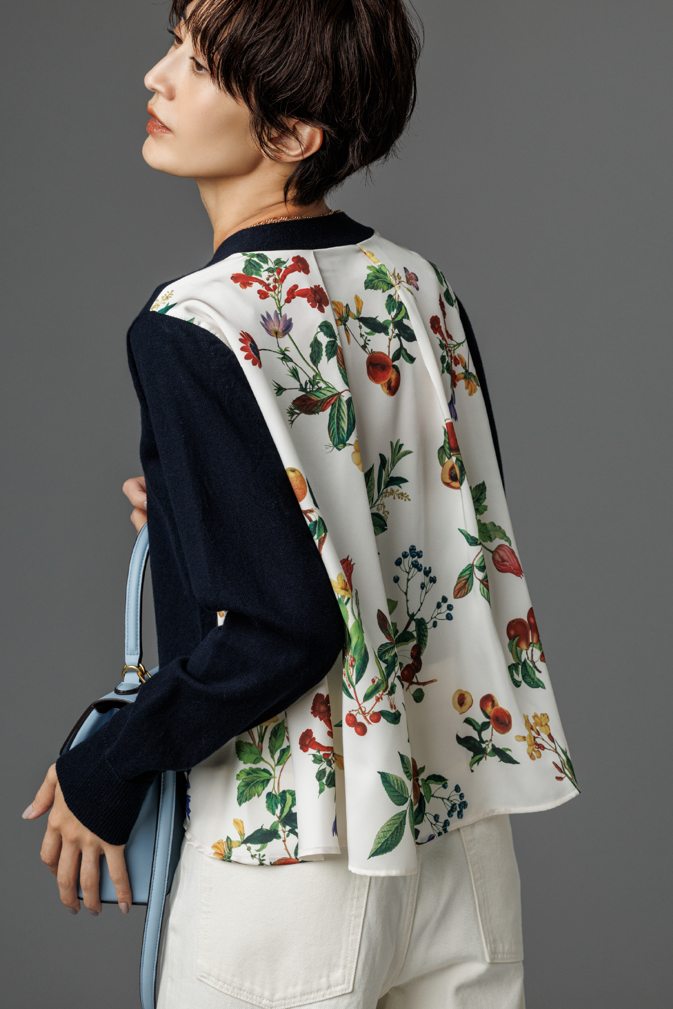 カシミヤコットンボタニカルドッキングカーディガン・細ベルト付きストレートデニムパンツ・ロングチェーンネックレス・メタルモチーフスクエアバッグを着用した女性