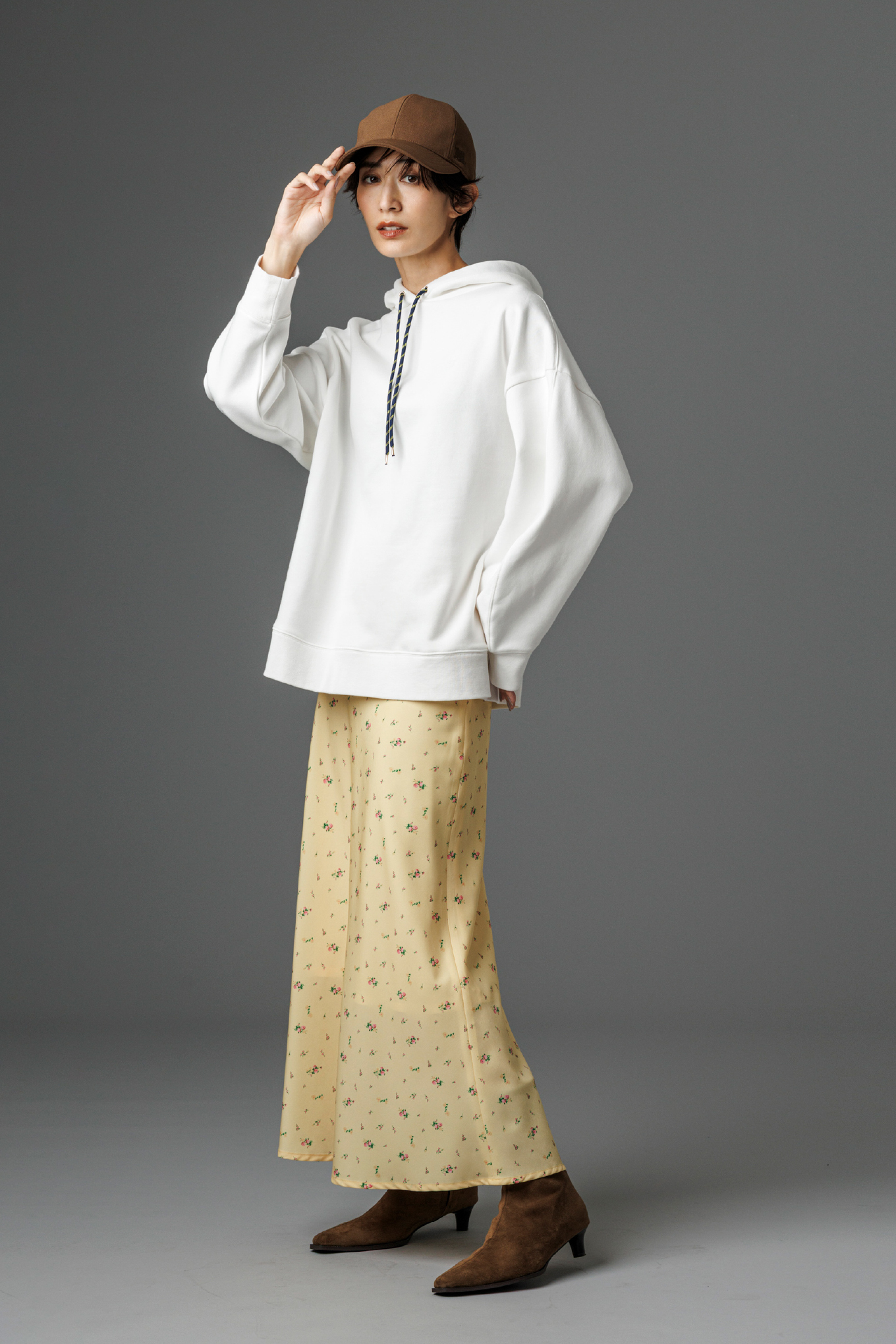 フォルムスリーブ裏起毛フーディー・小花柄プリントナロースカート・ポイントロゴ刺繍キャップ・キトゥンヒールショートブーツを着用した女性