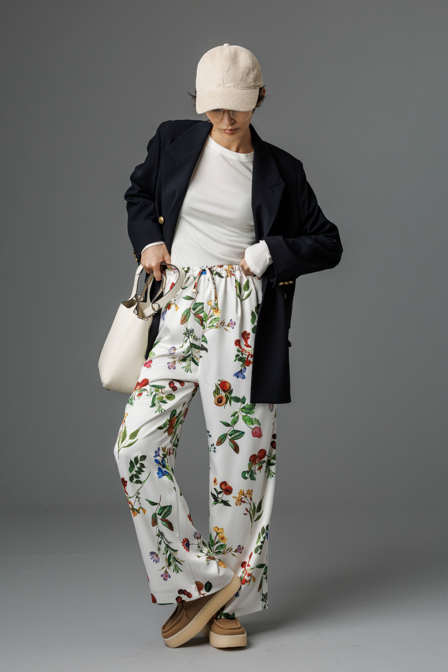 金釦ダブルブレストロングブレザー・ウールテンセルクルーネックシアーロンT・ボタニカル柄ウエストゴムイージーパンツ・M刺繍コーデュロイキャップ・2WAYハンド&ショルダーバッグ・レースアップシューズを着用した女性