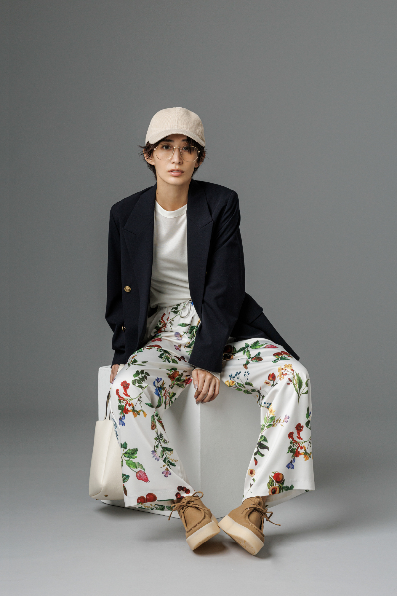 金釦ダブルブレストロングブレザー・ウールテンセルクルーネックシアーロンT・ボタニカル柄ウエストゴムイージーパンツ・M刺繍コーデュロイキャップ・2WAYハンド&ショルダーバッグ・レースアップシューズを着用した女性