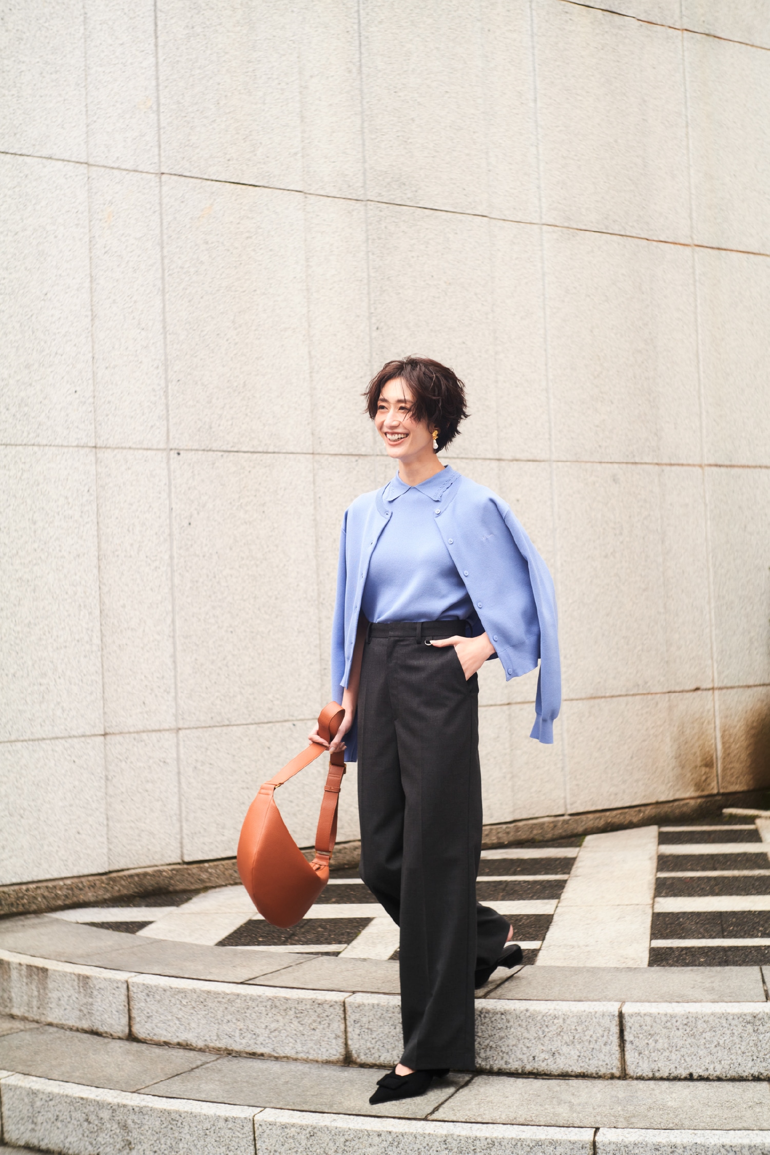 ブルーのクロップドフォルムカーディガンとスカラップレース衿ニットワンピース・チャコールグレーのテーラードトラウザー・メタルモチーフパールイヤリング・キャメルのボディバッグ・黒のバックル付きラムレザースリングパンプスを合わせた、エッジの効いたデザインが目を惹くコーディネート