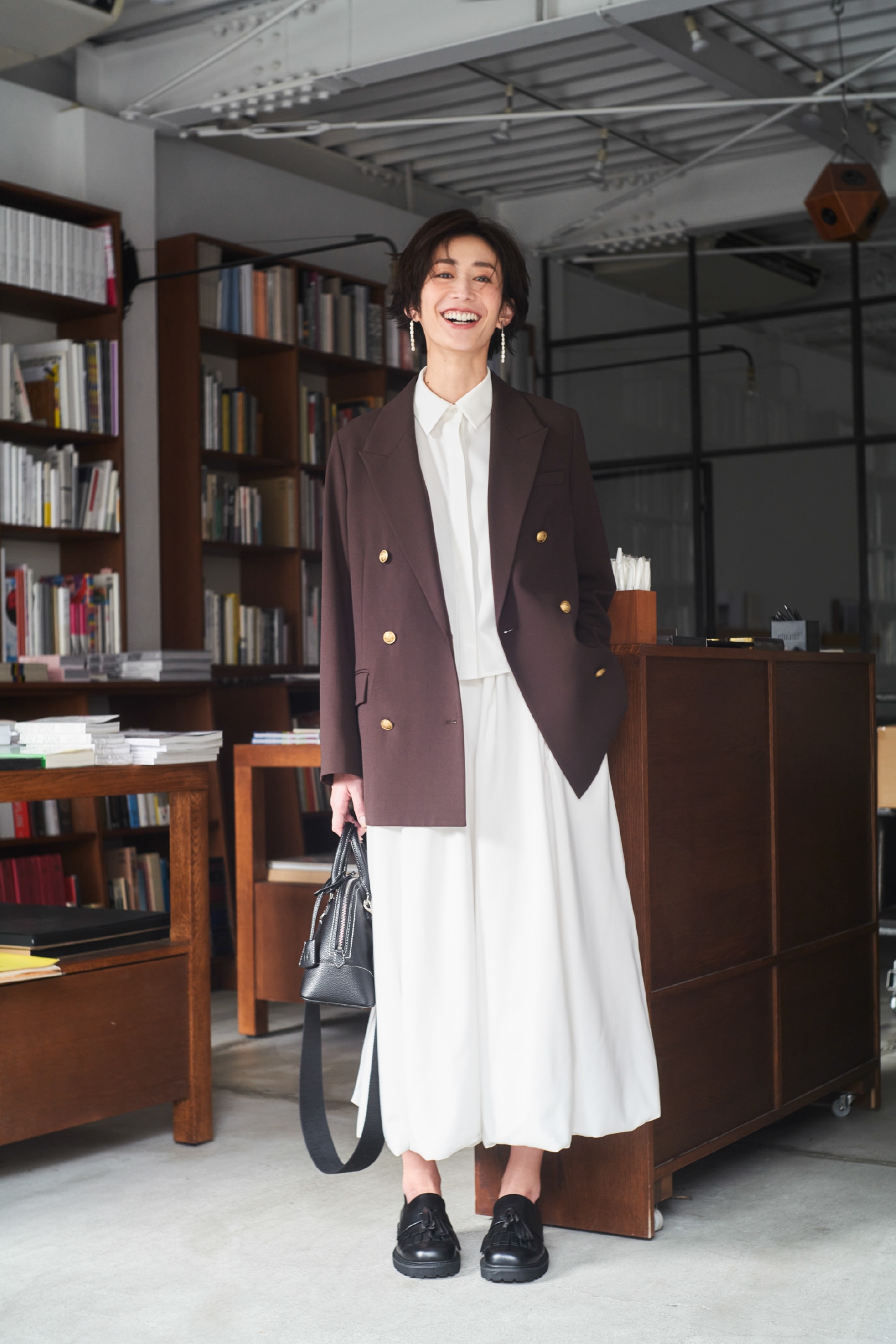 ブラウンの金釦ダブルブレストブレザー・アイボリーのリネン混バルーンシャツワンピース・メタルボールチャームイヤリング・黒のワイドショルダーミドルボストンバッグとタッセルローファーを合わせた、清潔感あふれるクリーンな素材が凛としたコーディネート