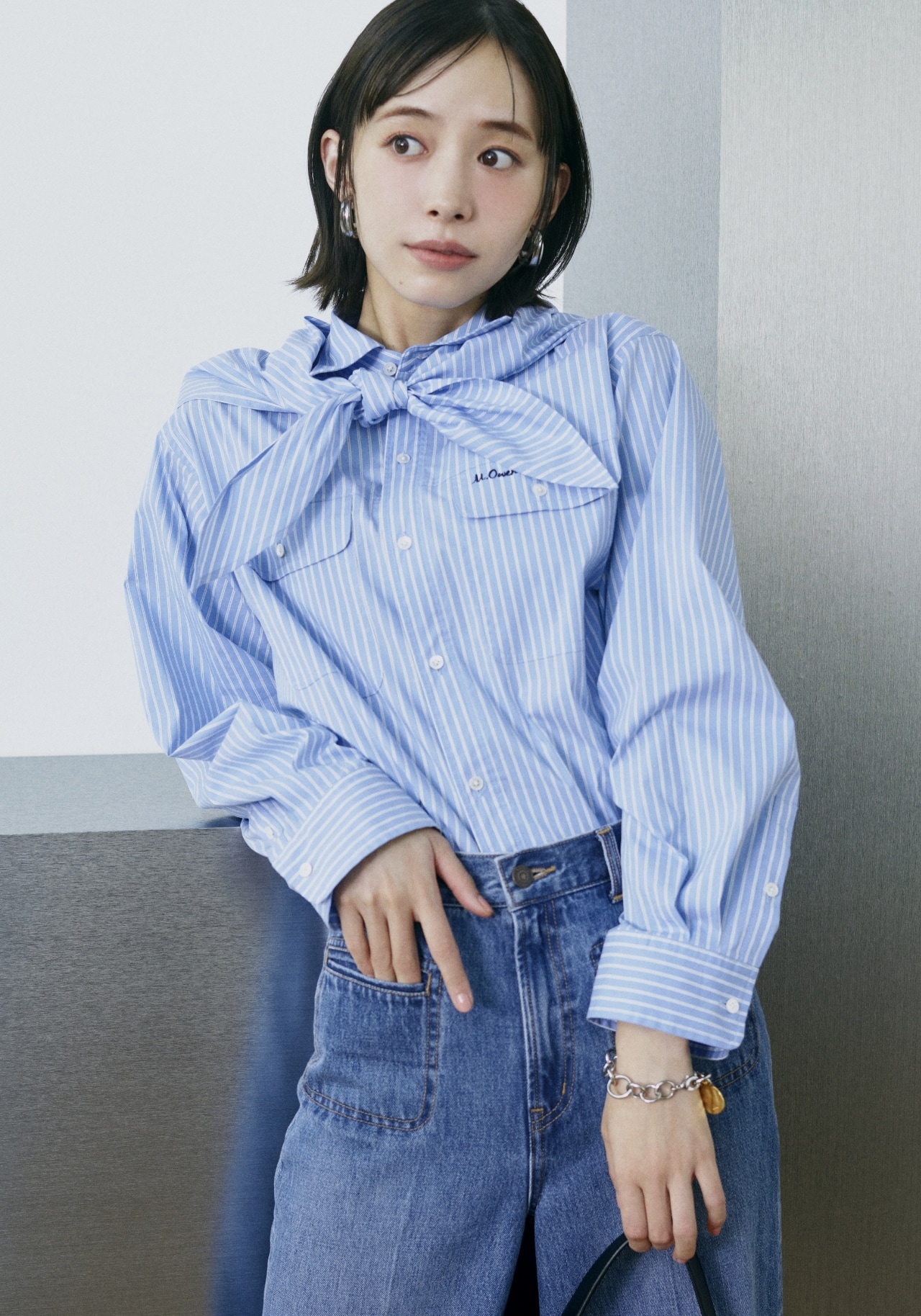 ブルーのスカーフ付きストライプワークシャツ・ライトブルーの玉縁ポケットセミフレアデニムパンツ・シルバーのメタルドロップフープイヤリング・ミックスのコインモチーフチェーンブレス・黒のボディバッグ・イエローのアンクルストラップパンプスを合わせたコーディネート