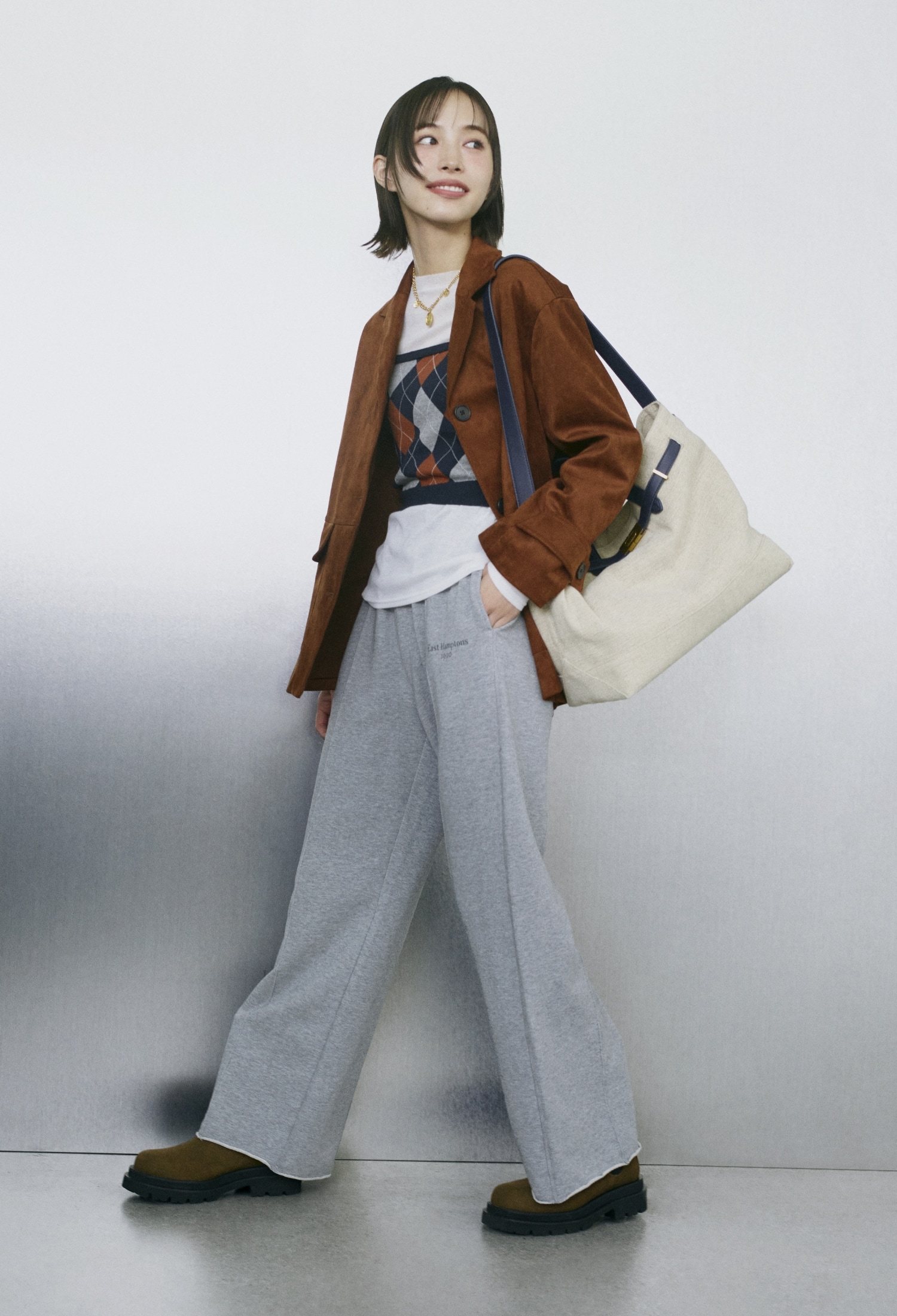 キャメルのリサイクルスウェードライクジャケット・白のウールテンセルシアーロンＴ・ネイビーのアーガイルニットチューブトップ・グレーのストレートスエットパンツ・ゴールドのモチーフチャームチェーンネックレス・ネイビーのベルト付きキャンバストートバッグ・モカのサイドゴアブーツを合わせたコーディネート