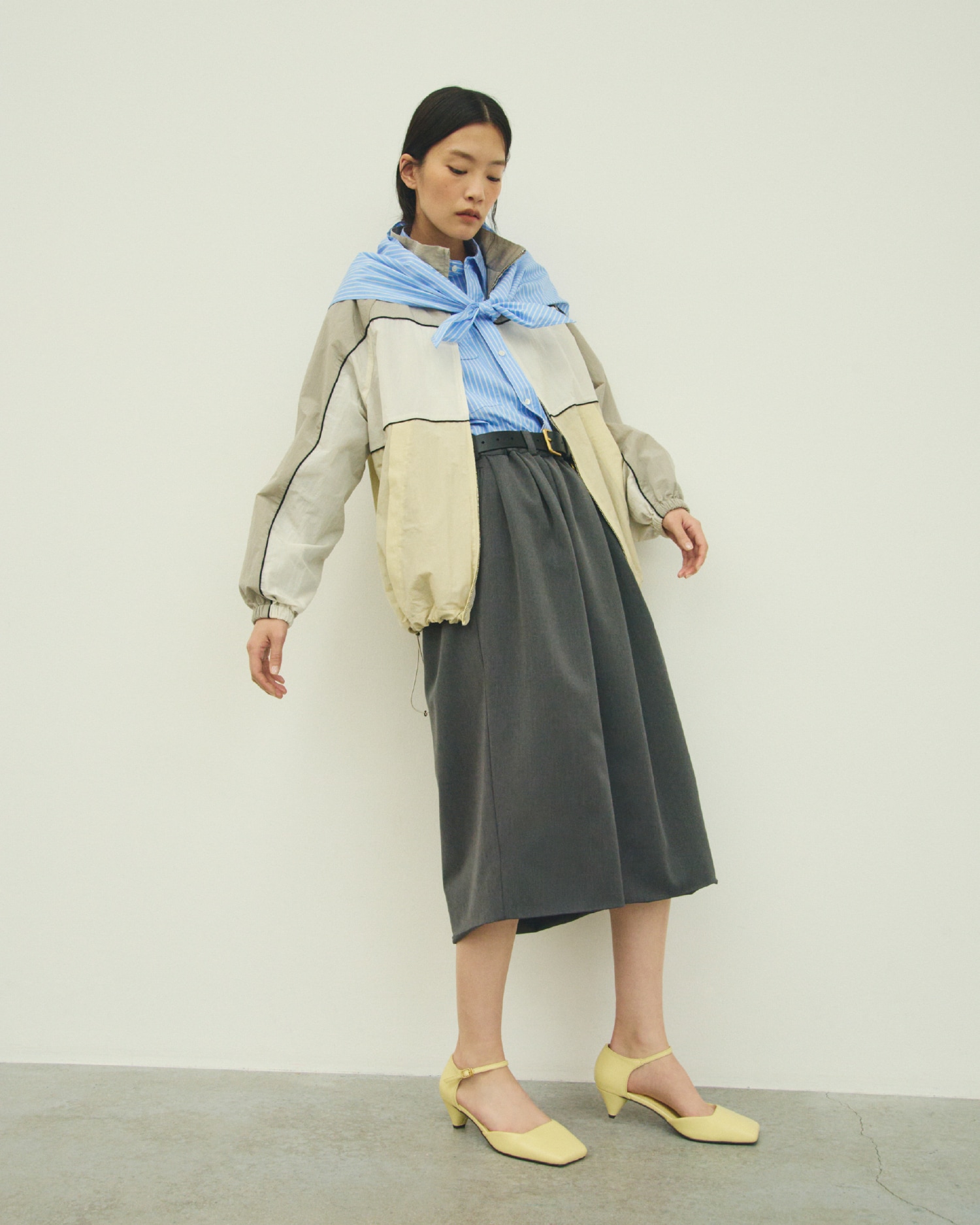 アイボリーのナイロントラックジャケット・ブルーのスカーフ付きストライプワークシャツ・グレーのウエストゴムランダムタックミディスカート・黒の撥水ナイロン２ＷＡＹワイドトートバッグ・イエローのアンクルストラップパンプス・ゴールドのスクエアダブルサルカンベルトを合わせたコーディネート