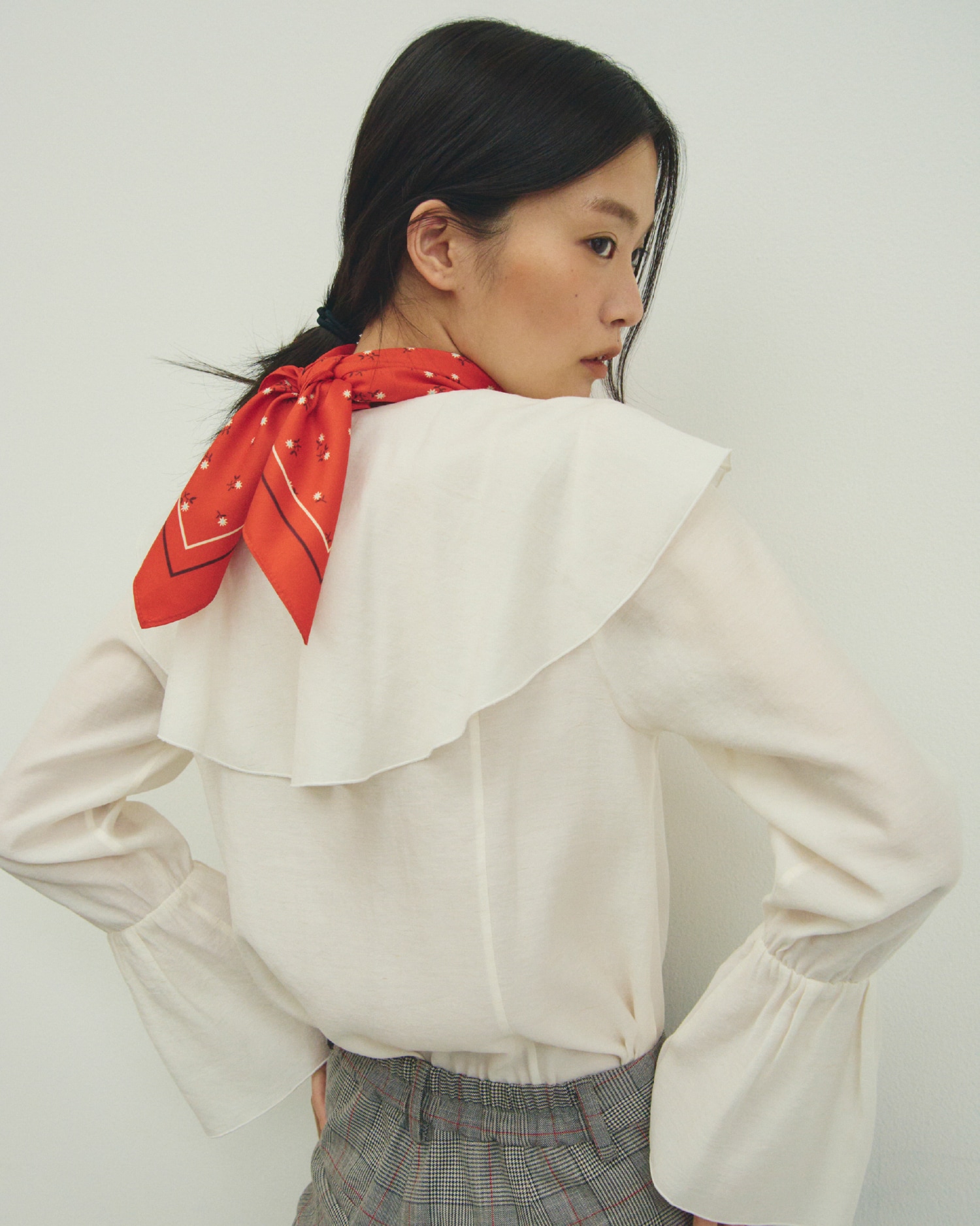 白のラッフルカラーシアーブラウス・チェック柄の４サイズチェックパンツ・赤の小花柄ラインスカーフ・ダークブラウンのショルダー付きボストンバッグとメッシュバレエを合わせたコーディネート