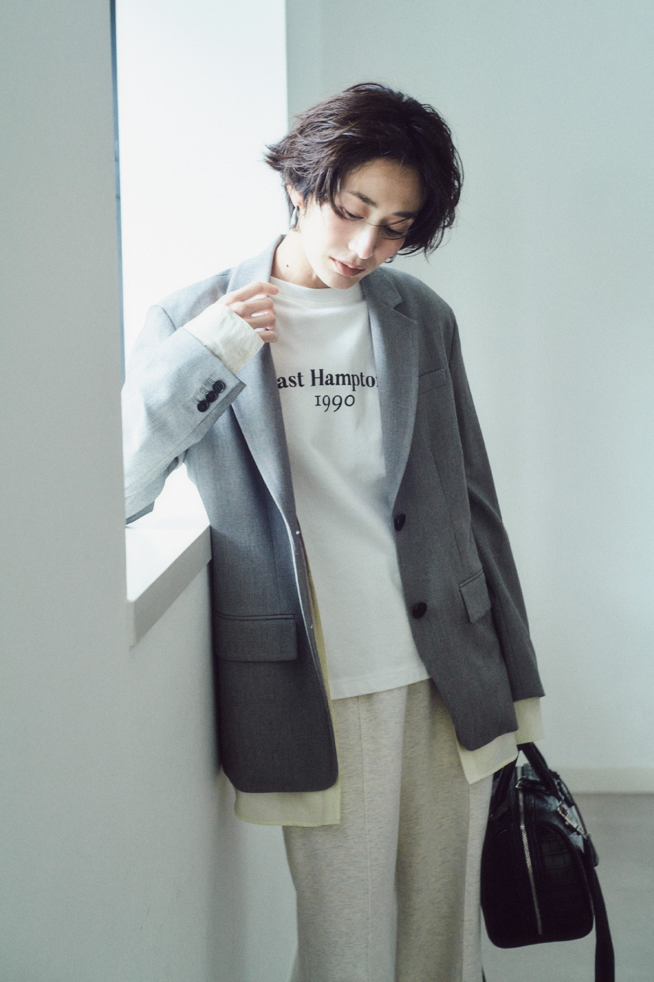 グレー色のシャツレイヤードＪＫ、ヴィンテージライクロゴＴシャツ、ストレートスエットパンツ、メタルドロップフープイヤリング、ショルダー付きボストンバッグを着用したモデル画像