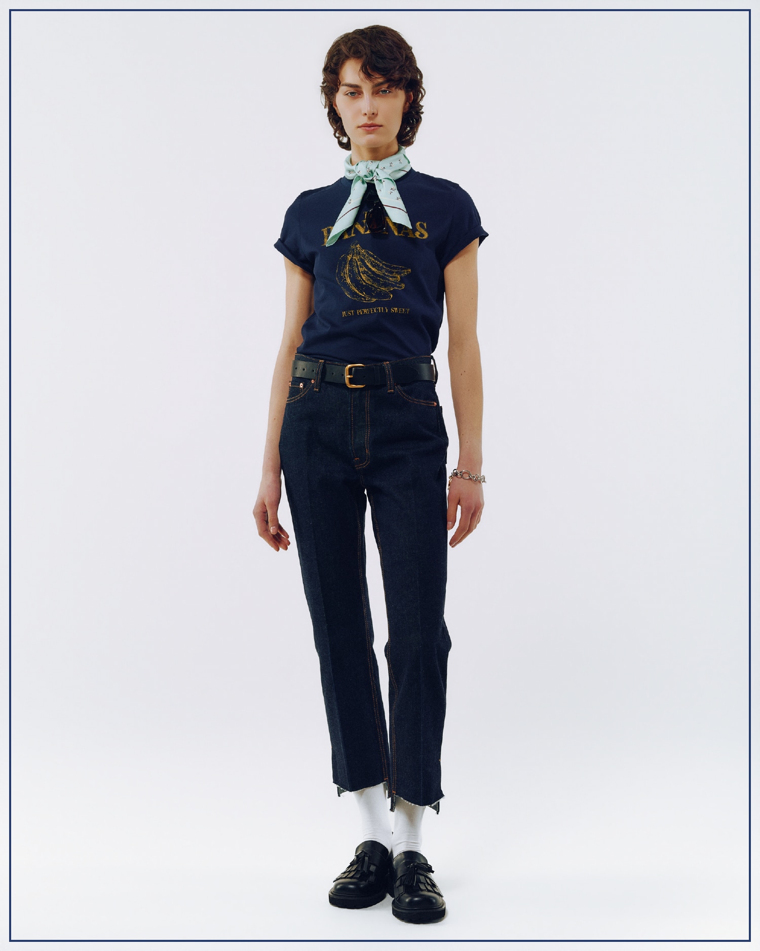 ネイビーのＴシャツ・インディゴの裾段差テーパードデニムパンツ・黒のサングラス・コインモチーフチェーンブレス・ライトブルーの小花柄ラインスカーフ・黒のタッセルローファーを合わせたコーディネート