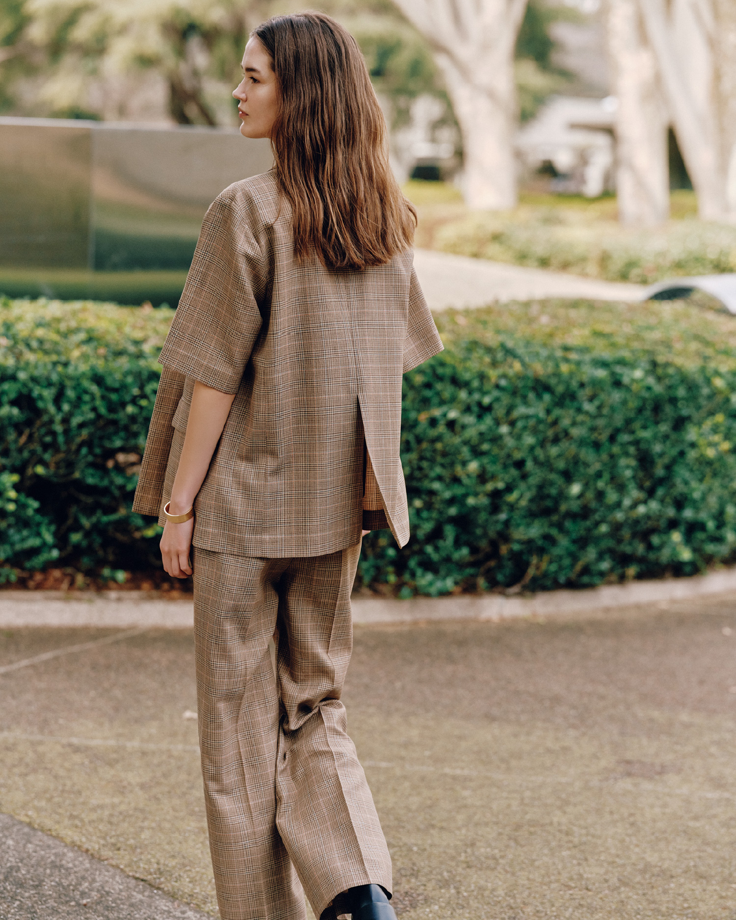 ブラウンチェックパターンのＵＶカット金釦ハーフスリーブＪＫ、カレッジＴシャツ、ＵＶカットノータックスラックスＰＴ、モカシンローファー、メタルボリュームイヤリング、カーブカラーバングルを着用したモデル画像