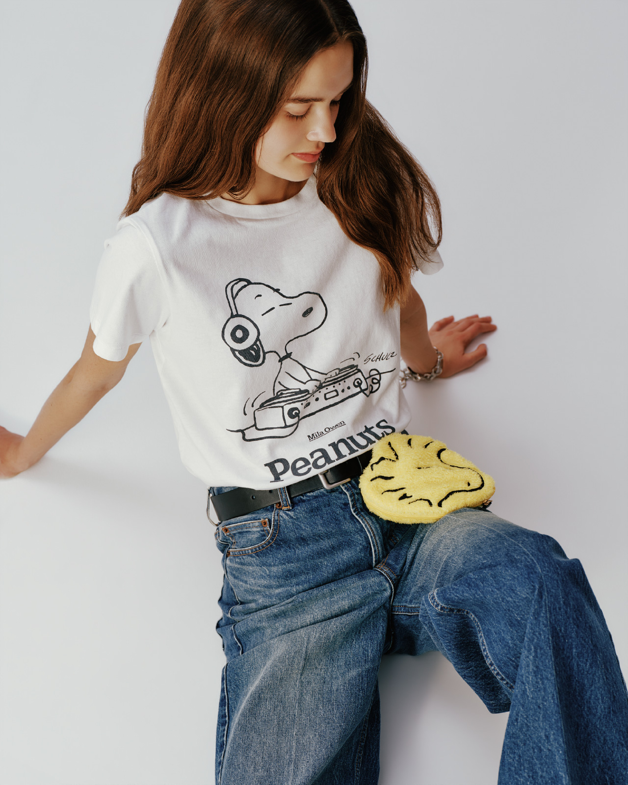 ＰＥＡＮＵＴコラボｓｎｏｏｐｙＴシャツ、バギーフレアデニム、ＰＥＡＮＵＴｓｎｏｏｐｙポーチチャーム、スクエアメタルサルカンベルト、タッセルチャームランダムチェーンベルト、カーブカラーバングル、コインモチーフチェーンブレスを着用して床に座ってる女性の画像