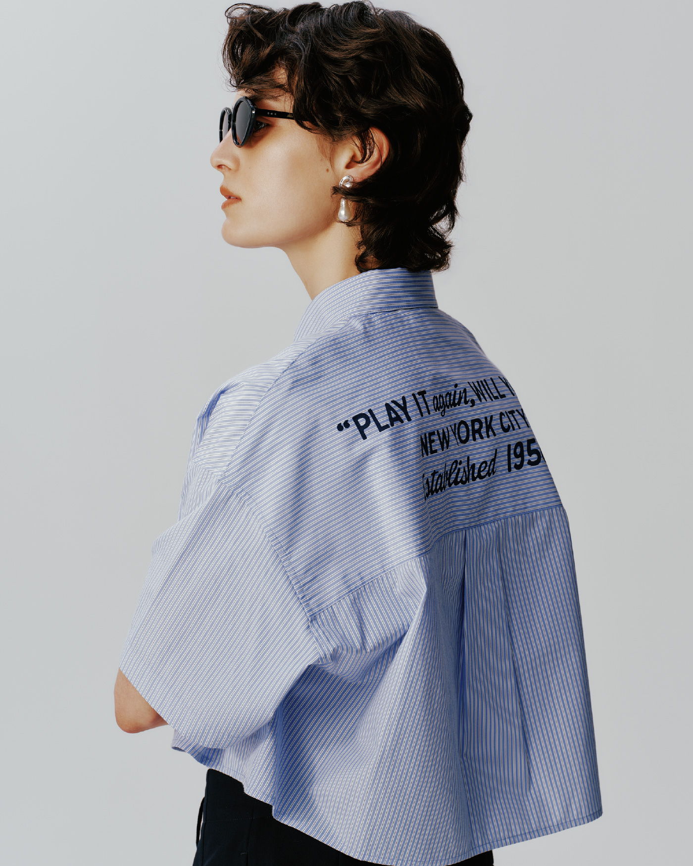 ＰＥＡＮＵＴコラボボタンダウン短丈シャツ、キャットアイサングラス、メタルモチーフパールイヤリングを着用した女性の画像