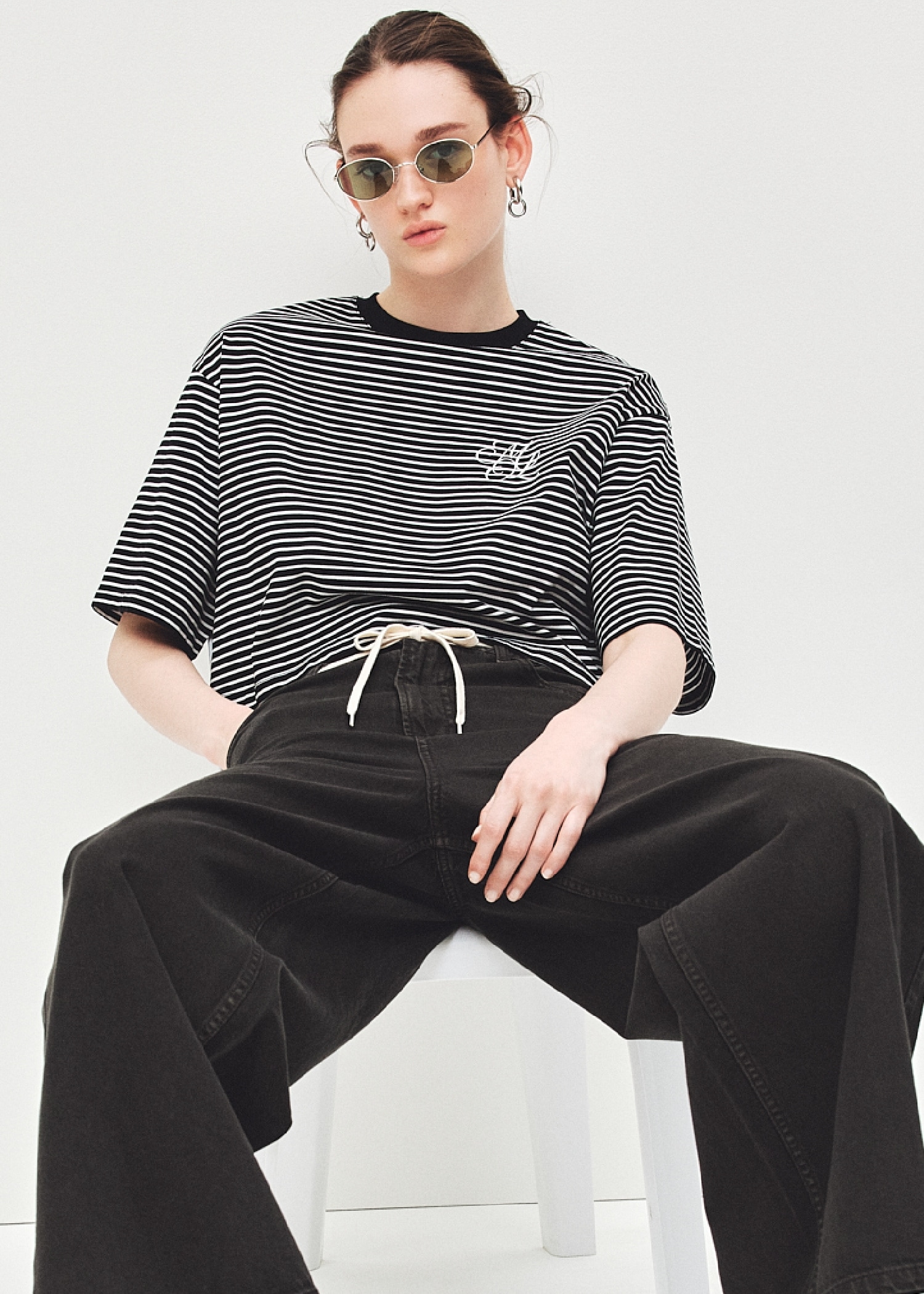 黒のハイラインモノグラムTシャツ・ダークブラウンのドロストイージーパンツ・グリーンオーバルカラーレンズサングラス・イヤリング・黒のモカシンローファーを合わせたコーディネート