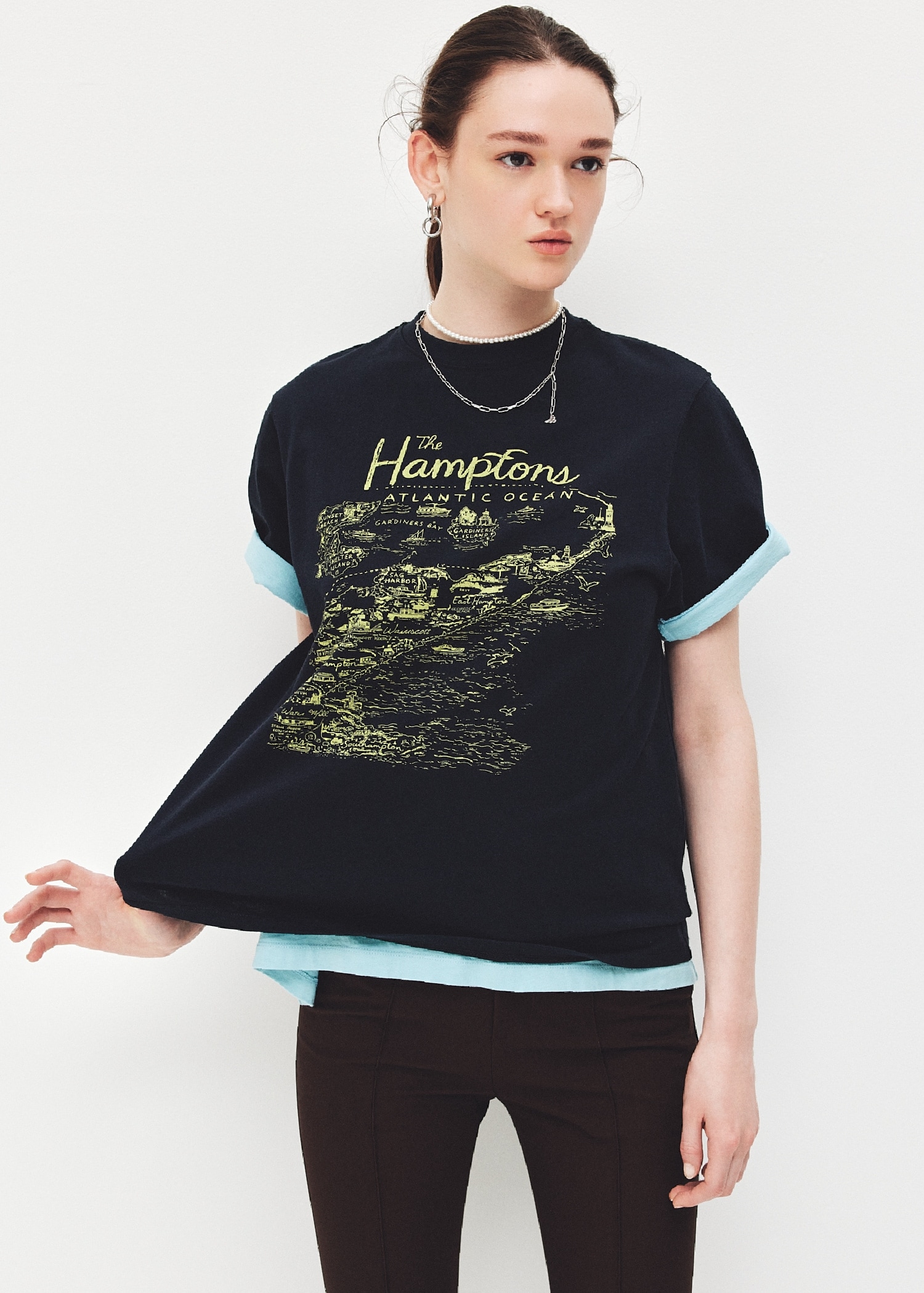 ネイビーのMap Pattern グラフィックTシャツ・ライトブルーのSAILING CLUBグラフィックTシャツ・ダークブラウンのカプリパンツ・イヤリングとネックレスを合わせたコーディネート