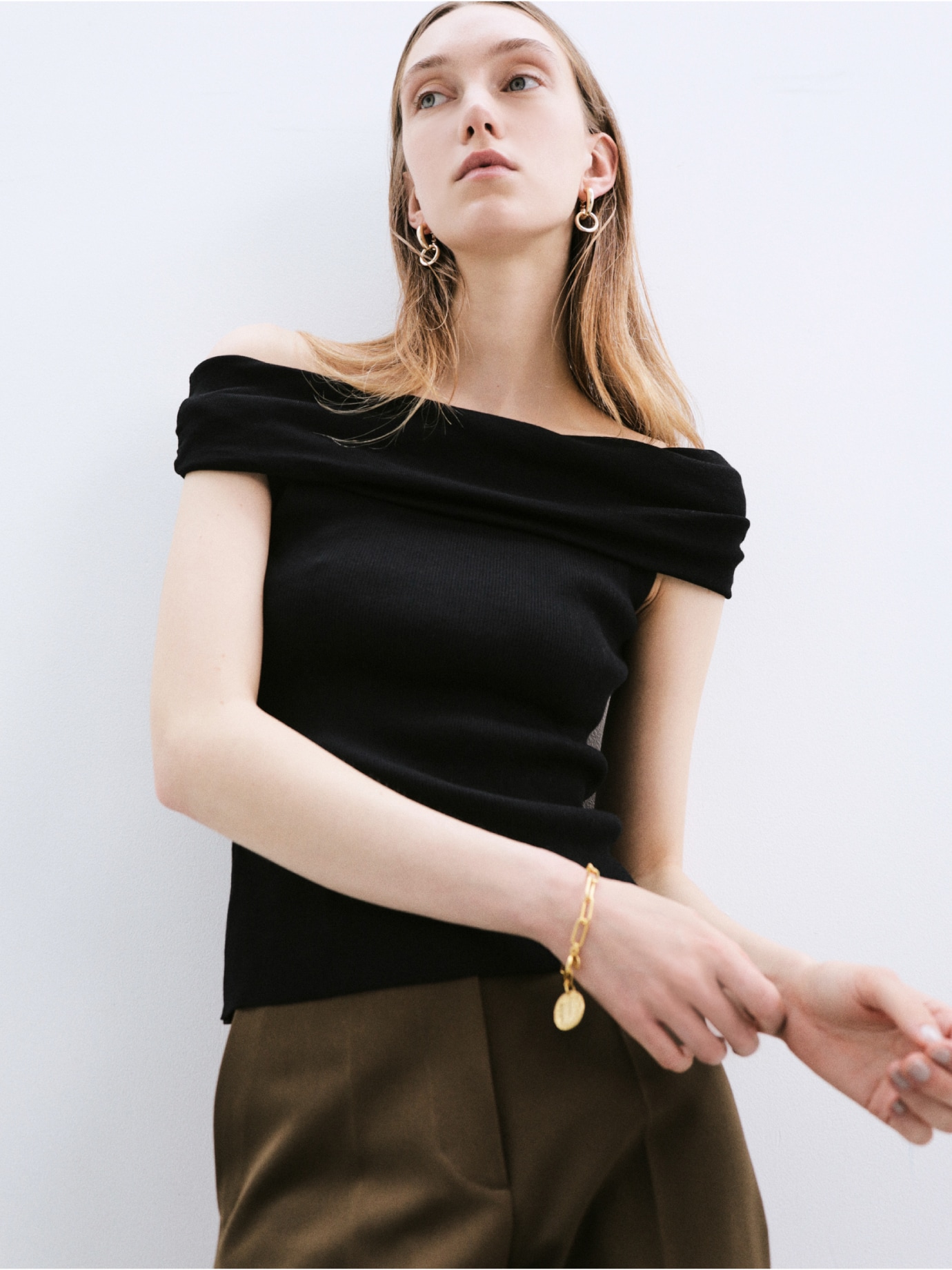 黒のクールタッチオフショルニット・ブラウンの４サイズパンツ・ゴールドのメタルクロスフープイヤリングと【EVERYDAY PROOF JEWELRY 】コインスクエアチェーンブレス・キャメルのストラップサンダルを合わせたコーディネート
